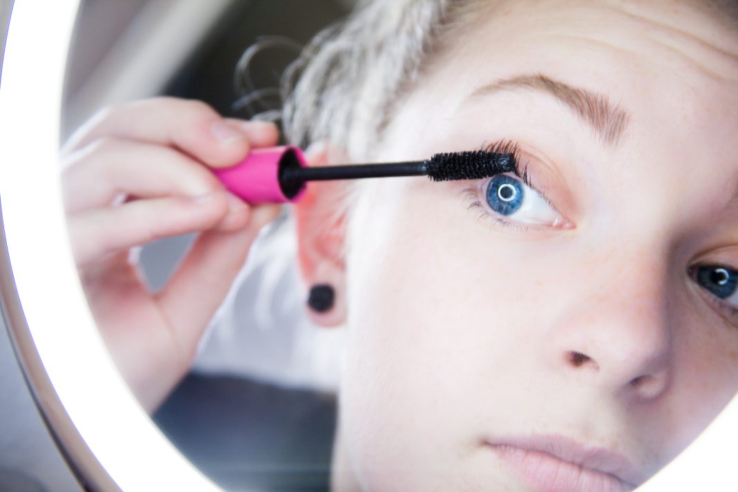 Femme appliquant du mascara devant un miroir, illustration de la tendance ghost lashes