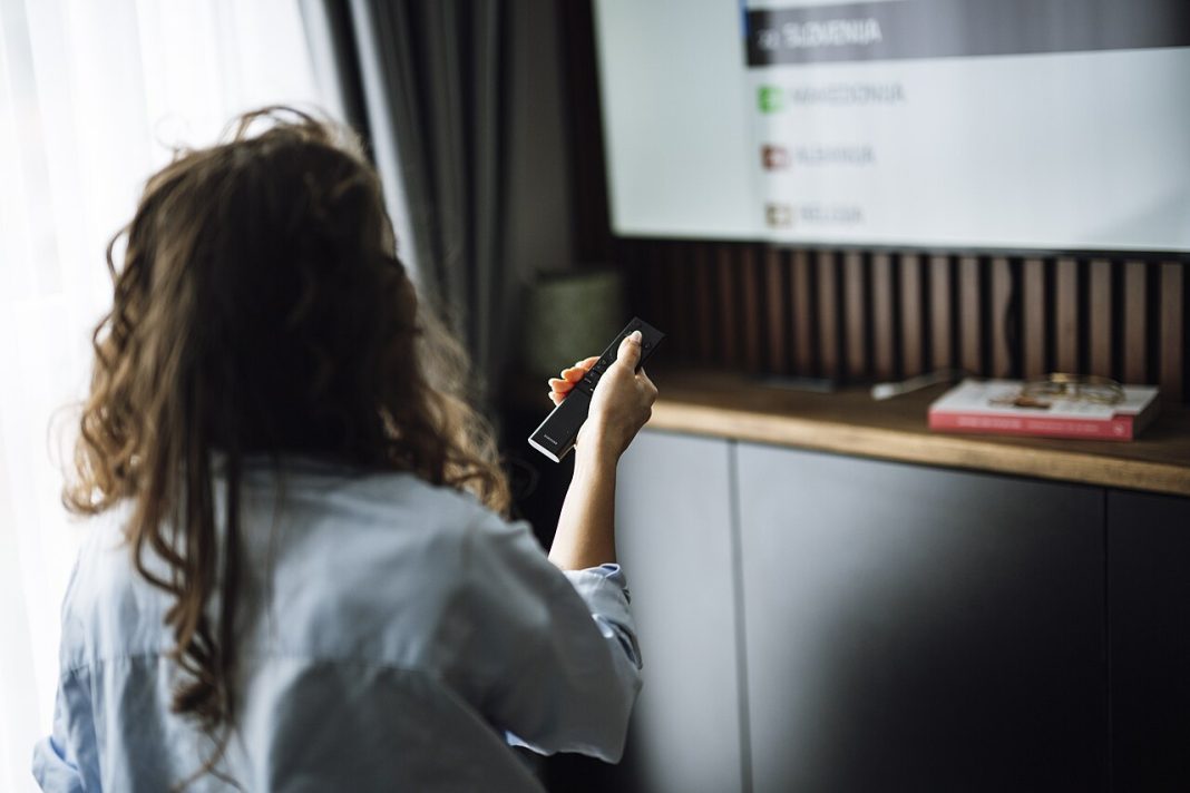 Personne assise sur un canapé regardant la télévision avec une télécommande