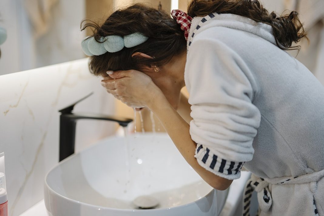 Personne se lavant doucement le visage au-dessus d’un lavabo pour illustrer une routine de soins simple
